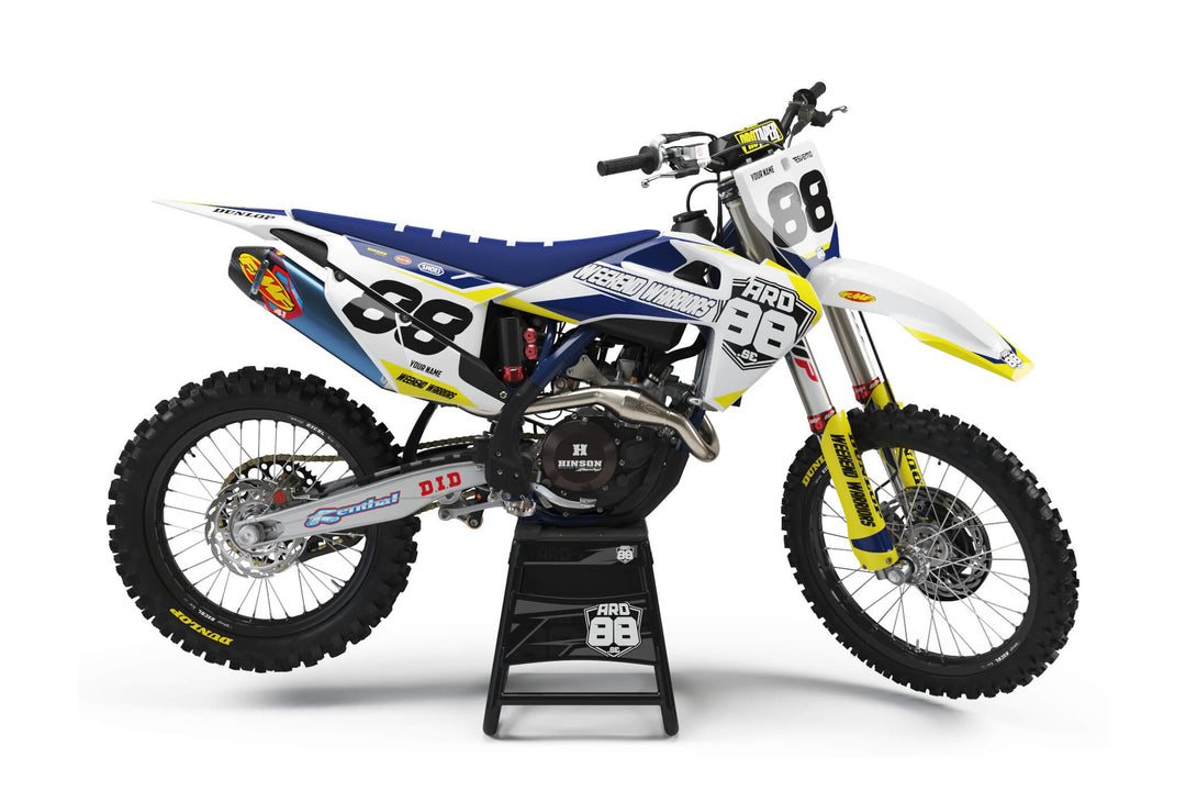 Husqvarna-crosshoj med dekalkitet Weekend Warriors – vit och mörkblå grafik med gula kilar, svarta siffror och namnet Weekend Warriors i trycket