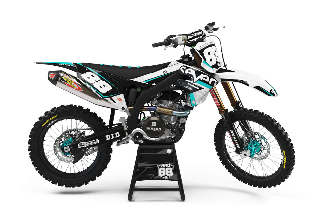Kawasaki crosshoj med dekalkit Seven T – svart och vitt med turkosa detaljer och vita siffror.