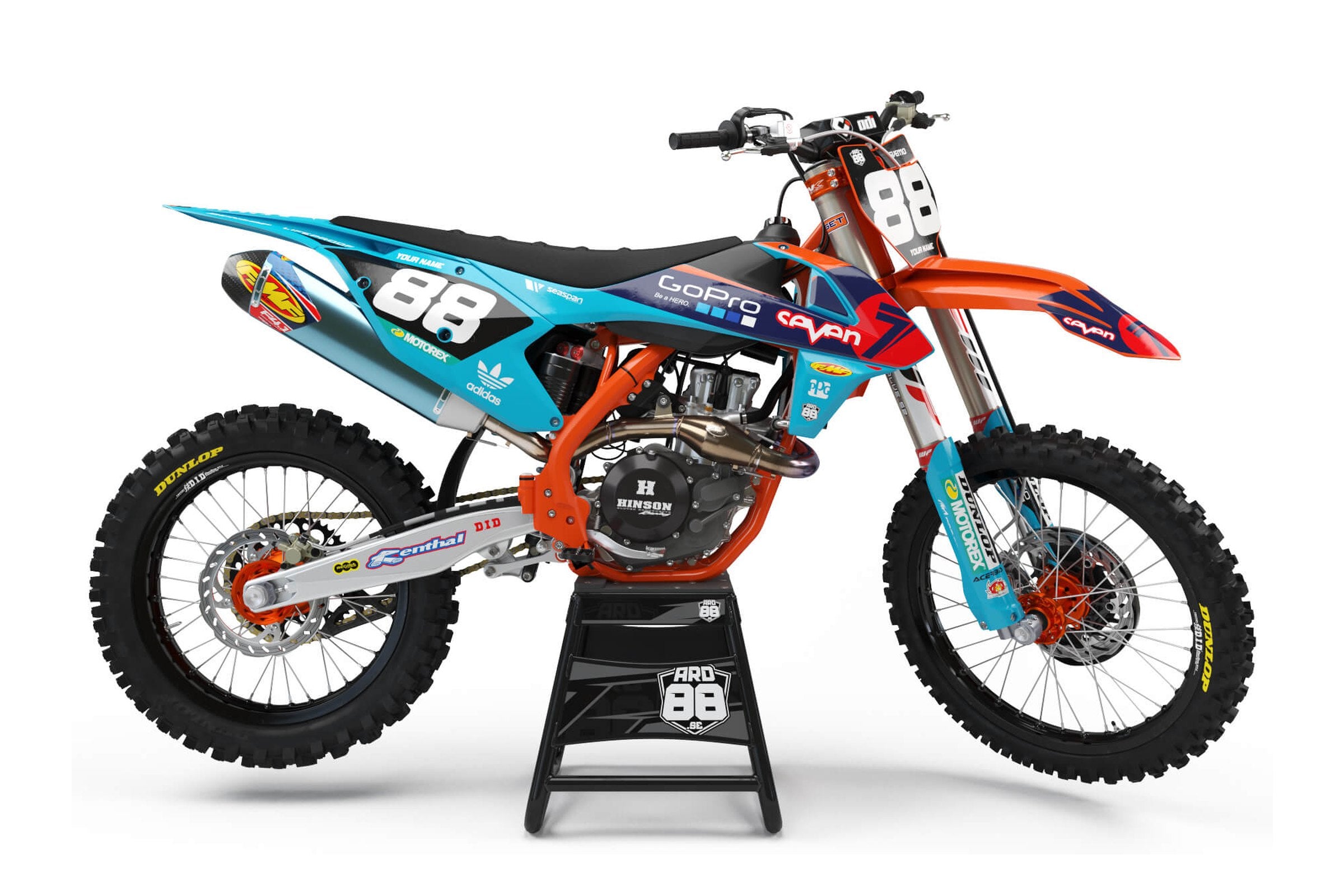 KTM-crosshoj med dekalkit Race Replica – turkos bak, orange fram och en mörkblå och röd pil i mitten, med vita siffror mot turkos.