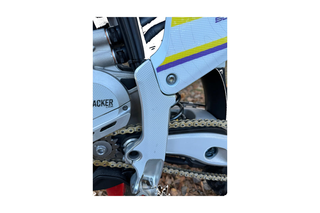 Närbild på en crosshojs ram där ett ljust, matt slitskyddsmaterial med fin rutstruktur följer formen, mot vita kåpor med gula och lila ränder